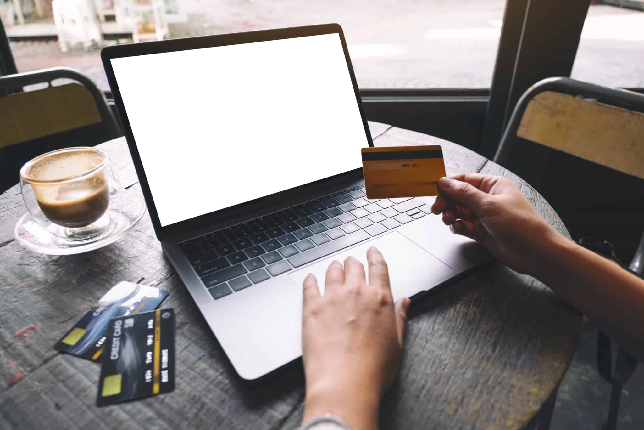 um ecrã de computador com mãos de homem a segurar cartão de crédito e monte de cartões de crédito ao lado na mesa